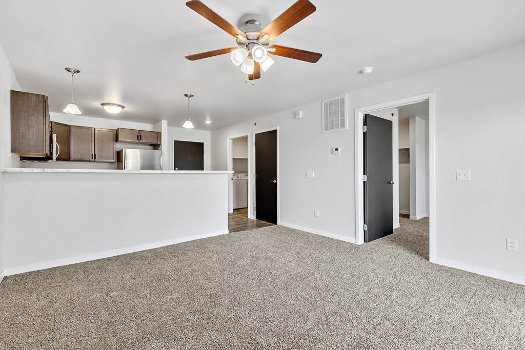 a living room with a ceiling fan and a kitchen in the background