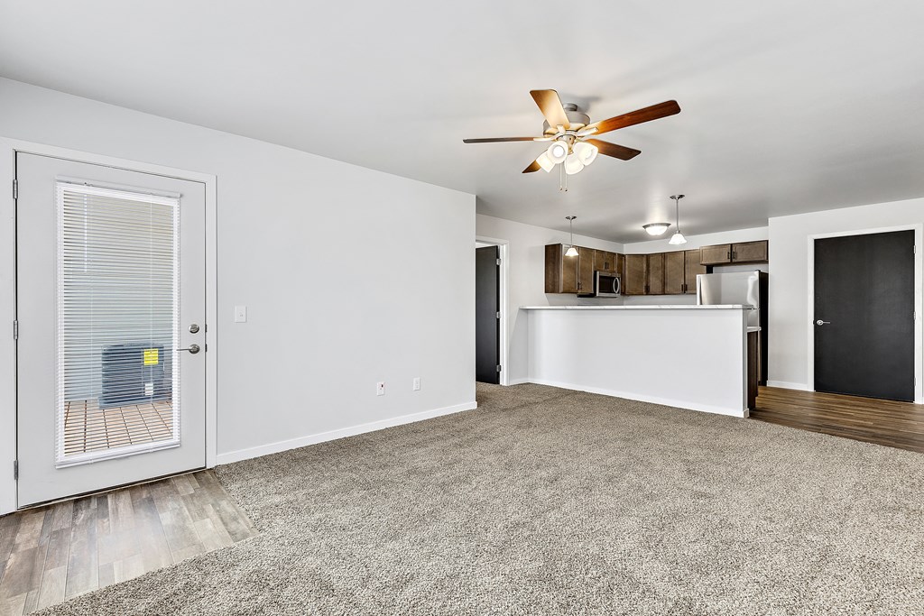 a living room with a ceiling fan and a kitchen in the background