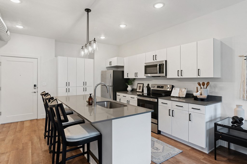 an open kitchen with white cabinets and a large island with black chairs at The Revival, Salt Lake City, UT