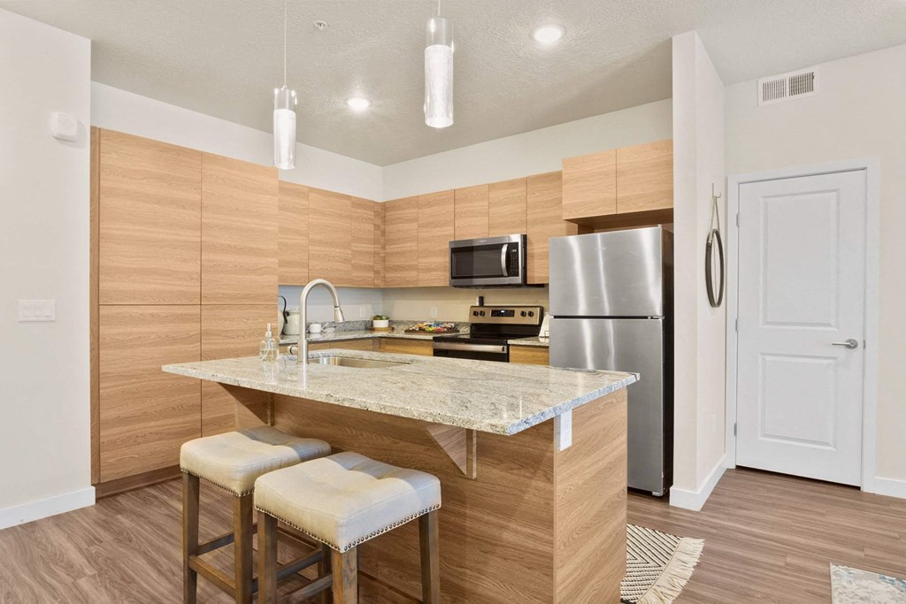 a kitchen with a large island with two stools in front of it at The Flats at Riverwoods, Utah, 84604
