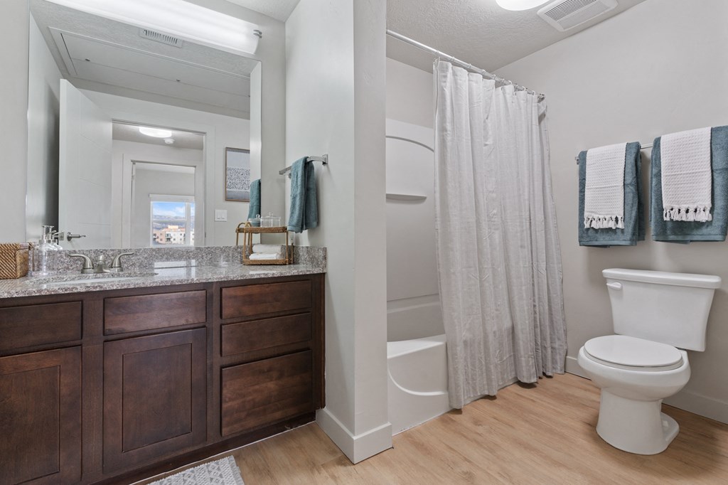 A white toilet sits next to a shower curtain in a bathroom. at Wilmington Flats Apartments, Utah