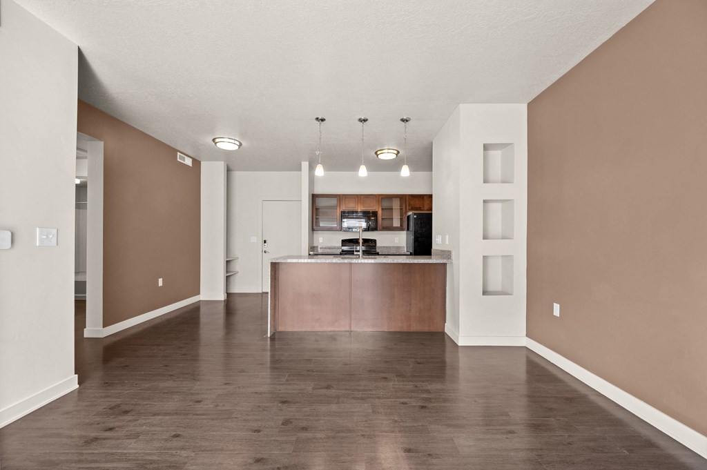 an empty living room with a kitchen in the background