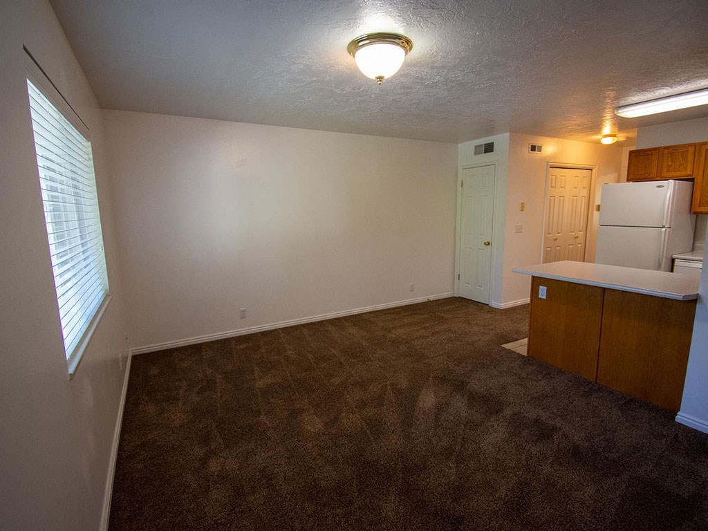 an empty living room with a kitchen and a refrigerator