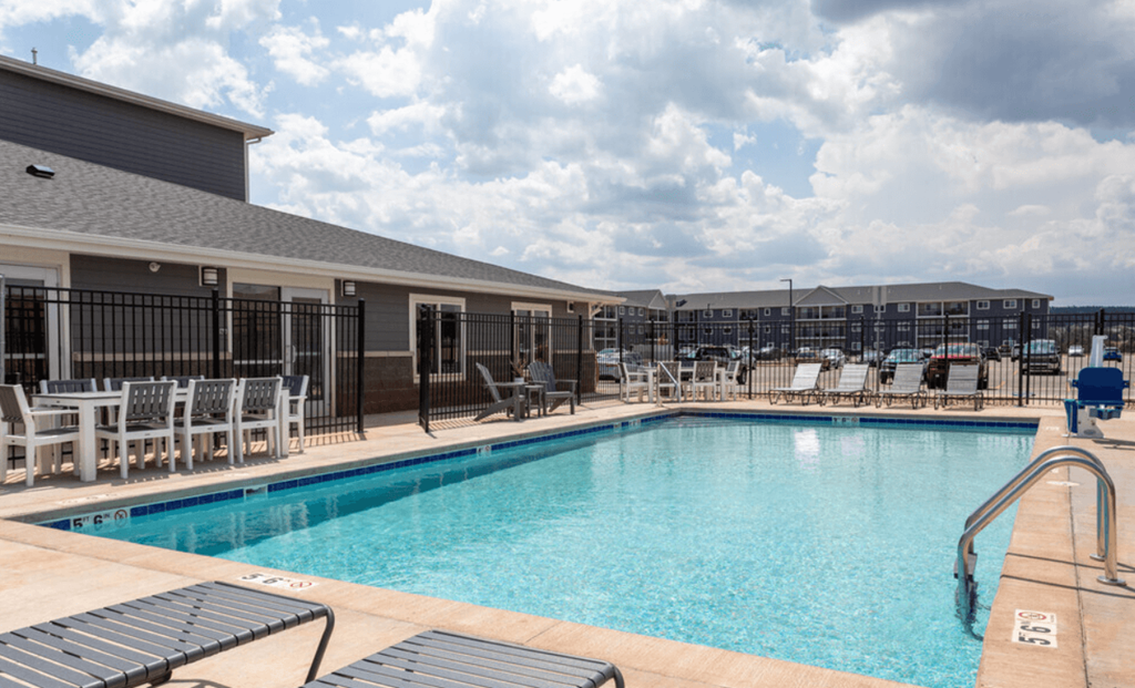 a swimming pool with lounge chairs and tables and a building in the background