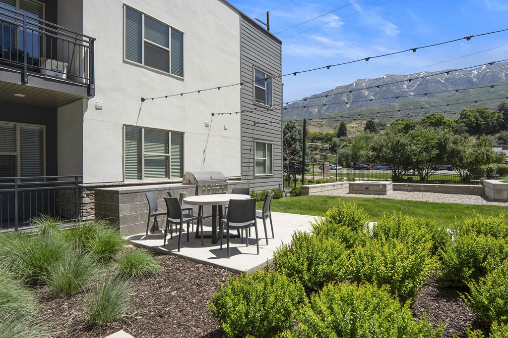 a patio with a table and chairs in front of a building at The Flats at Riverwoods, Provo