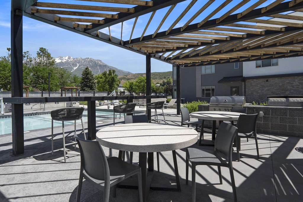 a patio with tables and chairs with a pool and mountains in the background at The Flats at Riverwoods, Provo, Utah