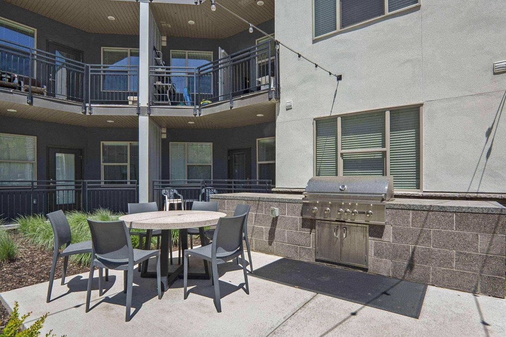 a patio with a table and chairs and a grill at The Flats at Riverwoods, Provo, Utah