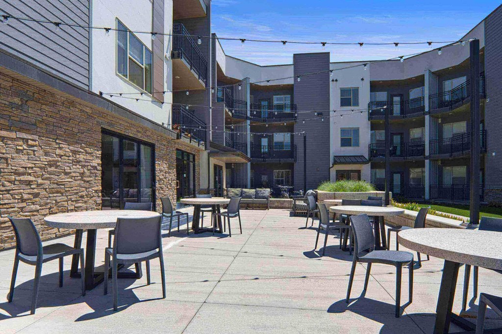 a patio with tables and chairs in front of an apartment building at The Flats at Riverwoods, Provo, 84604