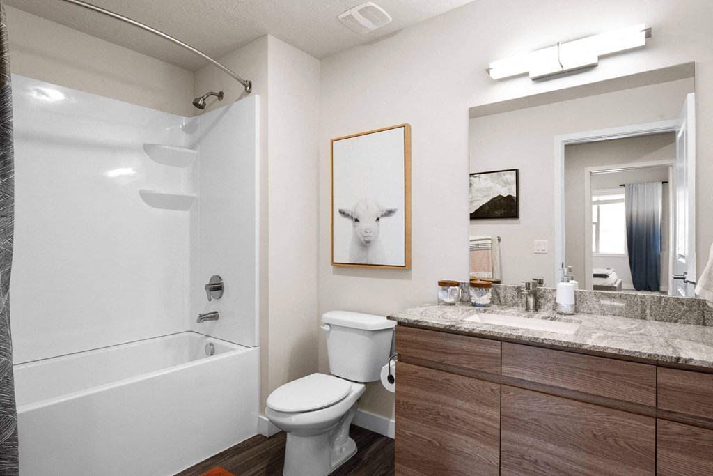 a bathroom with a white bathtub and a white toilet next to a sink with a mirror at The Flats at Riverwoods, Provo, UT, 84604