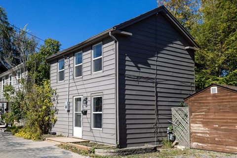 A grey house with a brown shed in front of it.