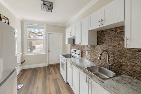 A kitchen with white cabinets and a stone backsplash.