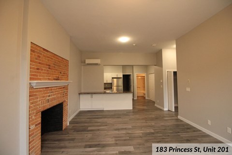 an empty living room with a brick fireplace and a kitchen