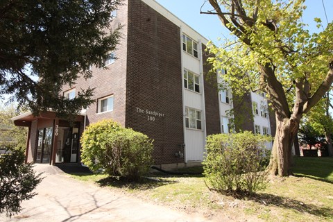 A brick building with a sign that says "The Sandpiper 300" is surrounded by trees and bushes.