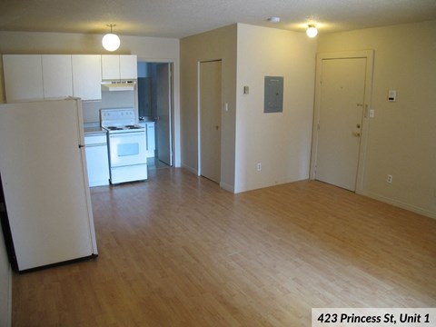 A kitchen with a refrigerator and oven in a room with wood floors and white walls.