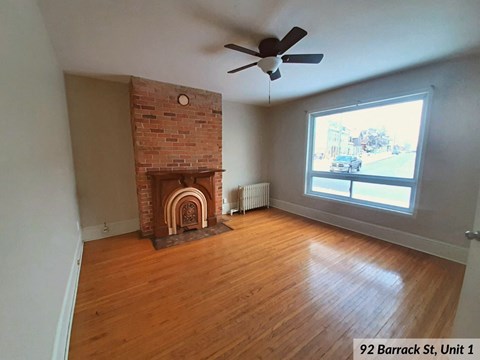 an empty living room with a brick fireplace and a ceiling fan