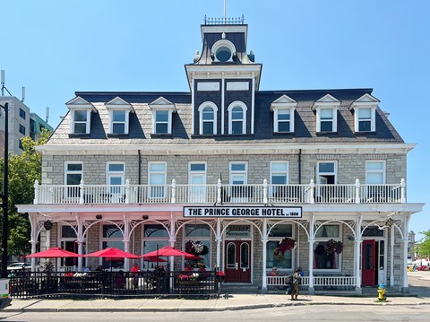 The Prince George Hotel is a historic building with a balcony and red umbrellas.