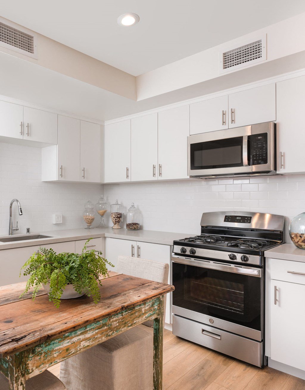 a white kitchen with stainless steel appliances and a wooden table