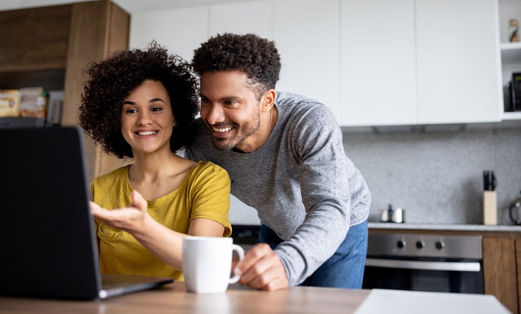a man and woman looking at a laptop computer in a kitchen