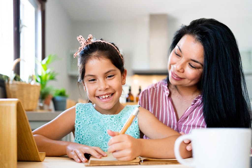 a woman and a girl sitting at a table using a laptop
