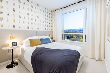A bedroom with a bed, a table with a lamp, and a window with a view.