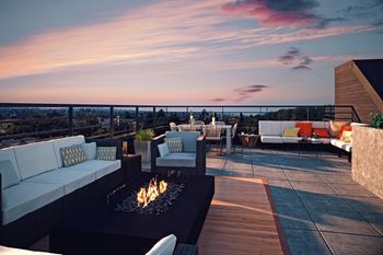 A patio with a fire pit and seating area overlooking a cityscape at dusk.