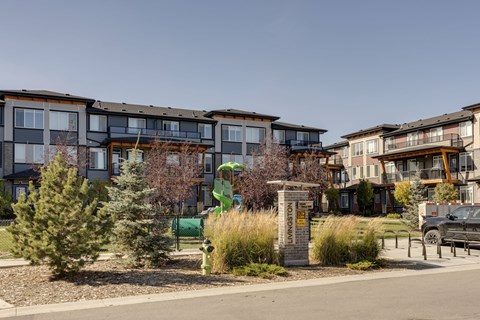 A row of modern townhouses with a green lawn and trees in the foreground.