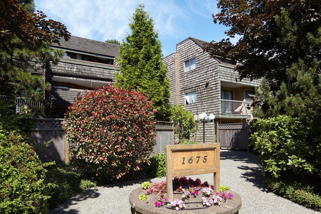a yard with a sign and flowers in front of an apartment building