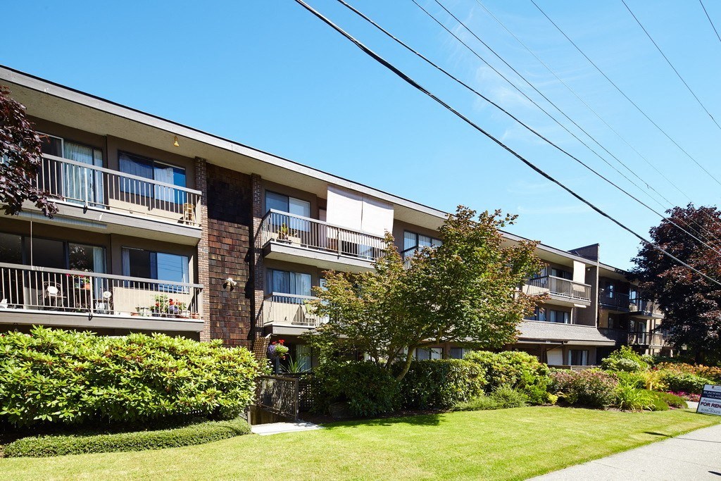 a picture of an apartment building with a green lawn and trees in front of it