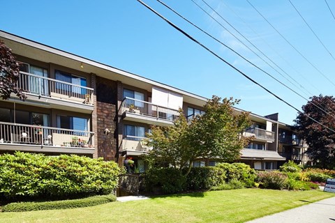 a picture of an apartment building with a green lawn and trees in front of it