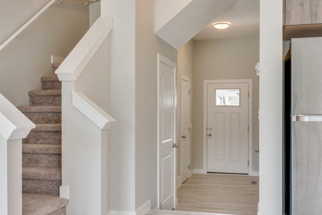 a hallway with a white door and stairs in the background