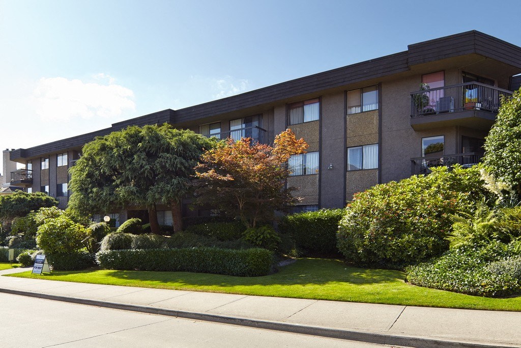 a large apartment building with a lawn and trees in front of it