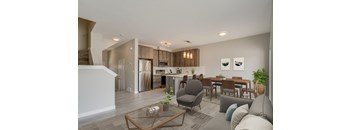 A modern living room with a grey sofa, a glass coffee table, and a dining table with chairs.
