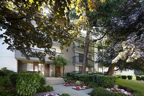 the exterior of an apartment building with a gravel driveway and trees