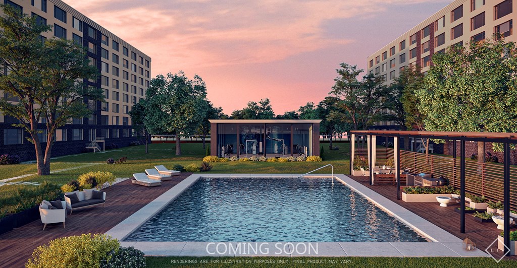 A pool surrounded by a deck and trees with a building in the background.