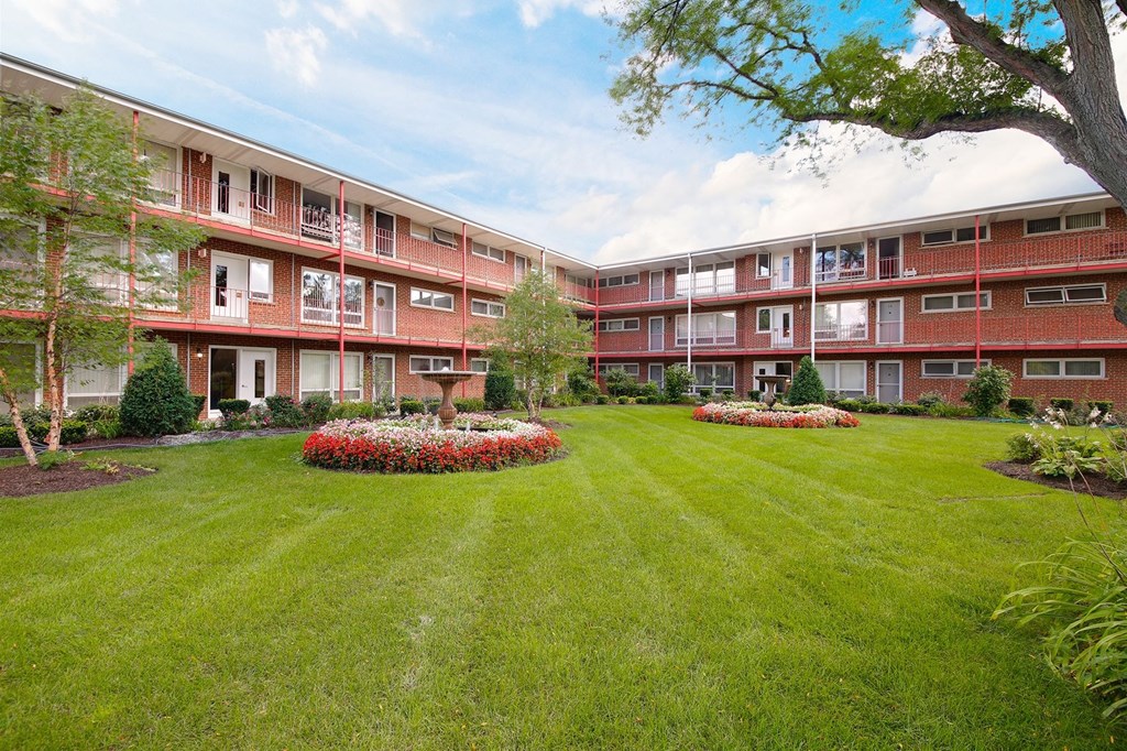 a courtyard with grass and flowers in front of an apartment building