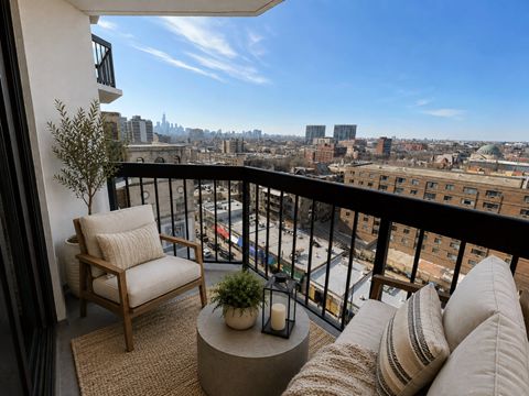 A balcony with a chair, cushions and a table with a plant and candle.