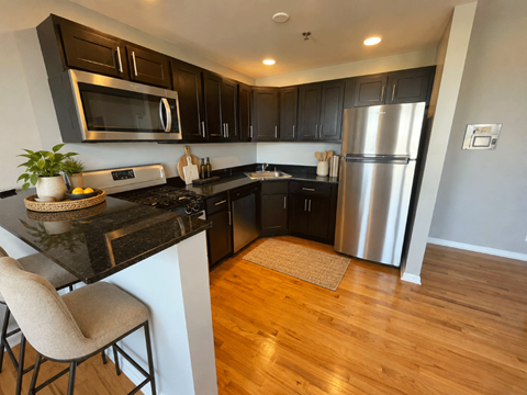 A kitchen with a black counter top and a stainless steel refrigerator.