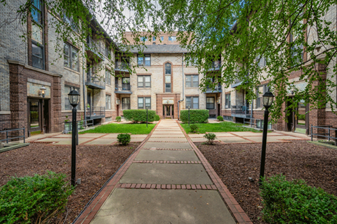 A courtyard with a brick pathway and a building in the background.