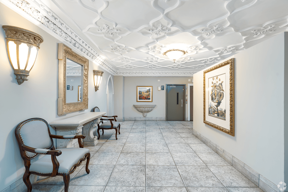 A hallway with a chair, a table, and a painting on the wall.