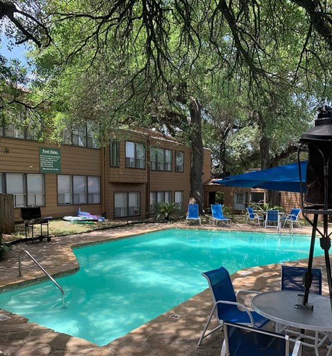 A pool surrounded by trees and chairs.
