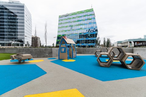 A playground with a blue and yellow surface and a green building in the background.