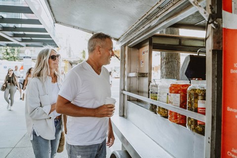 A man and a woman are standing in front of a food truck.