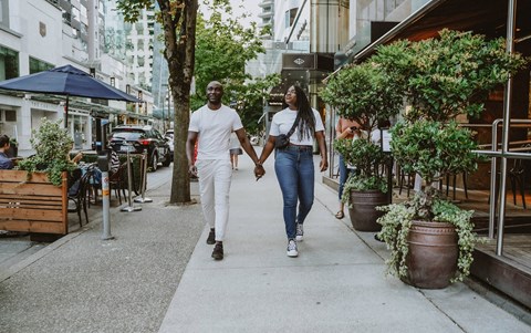 A man and a woman are walking hand in hand down a sidewalk.