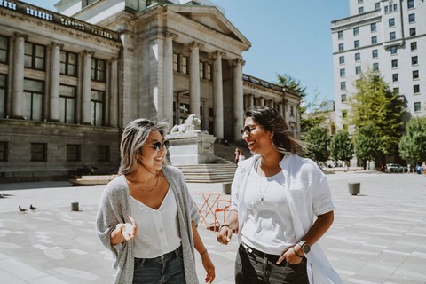 Two women walking and talking in front of a building.
