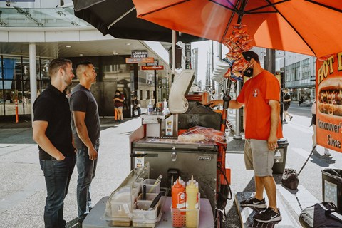 A man in an orange shirt is cooking food on a portable grill.