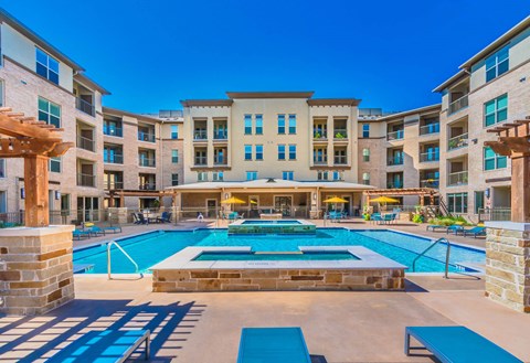 A large swimming pool in front of a multi-story apartment building. at Atlas Point at Prestonwood Apartments , Carrollton, Texas