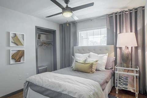A bedroom with a bed, a ceiling fan, and a nightstand with a lamp.