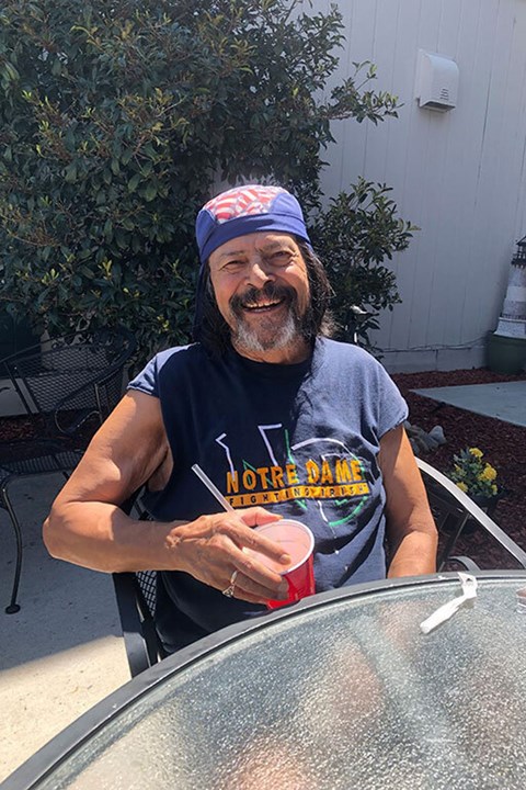 A man with a beard and a bandana on his head is sitting outside and holding a red cup.