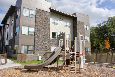 A playground with a slide in front of a modern building.
