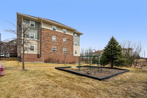 A playground with a swing set in front of a brick apartment building.